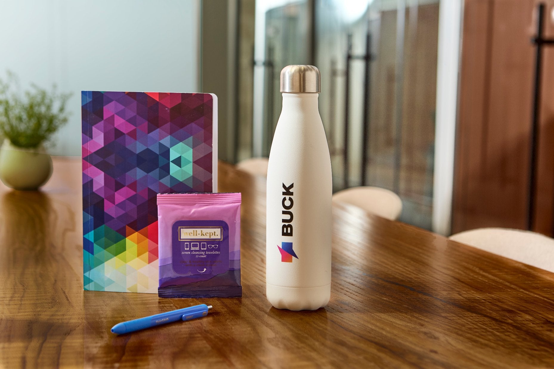 Branded water bottle, pen , tech wipes, and journal on wooden office table