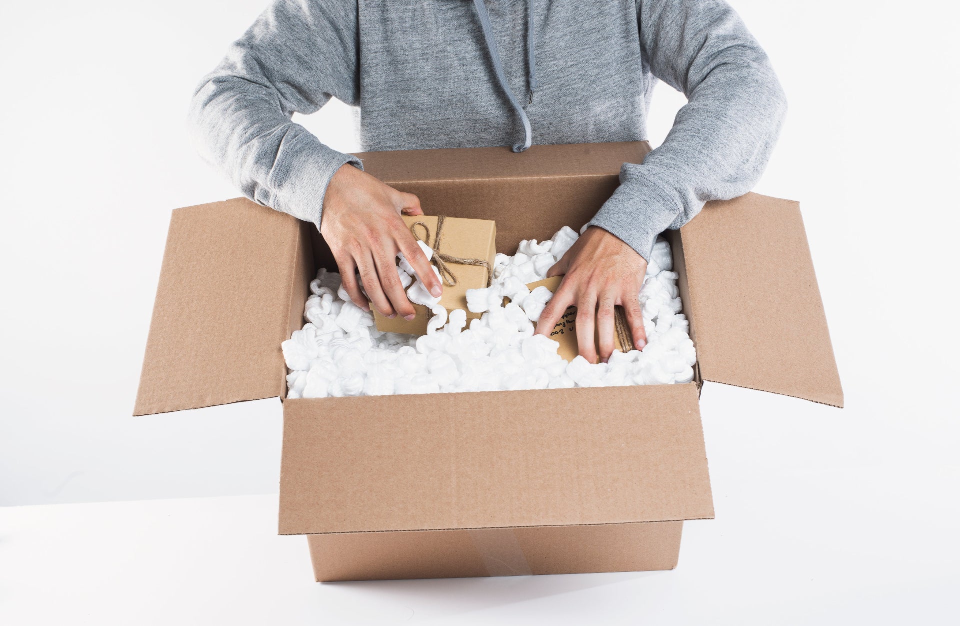 man packing cardboard box with packing peanuts and gifts